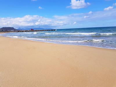 Weiter Sandstrand mit sanften Wellen, blauem Himmel und vereinzelten Wolken am Horizont.