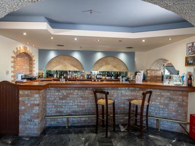 Gemütliche Hotelbar mit steinverklehrtem Tresen, Holzhockern und eingebauten Regalen.