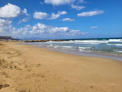 Ein weiter Sandstrand mit blauem Himmel, weißen Wolken und sanften Wellen am Meer.