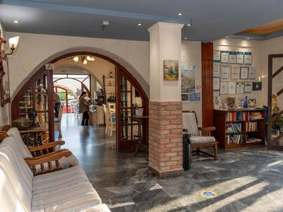 Pasillo de hotel bien iluminado con asientos, estantería y vista hacia la entrada