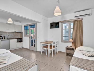 Helles Hotelzimmer mit zwei Einzelbetten, Essbereich, Küchenzeile und Balkon mit Meerblick.