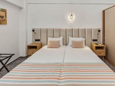 Modernes Hotelzimmer mit zwei weißen Betten, gepolstertem Kopfteil und Nachttischen.