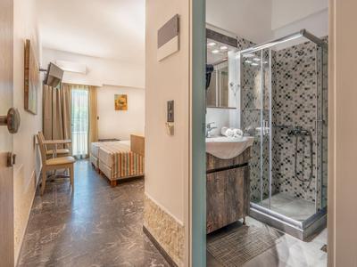 Blick durch einen Flur auf ein helles Hotelzimmer mit Bett und angrenzendem Badezimmer mit Dusche.
