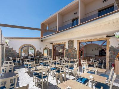 Terrasse eines Hotels mit Tischen, Stühlen und mediterranem Baustil bei klarem Himmel.