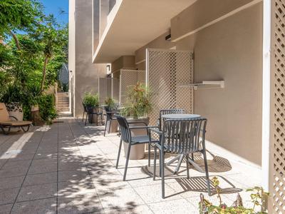 Terrasse mit Tisch und Stühlen vor einem Hotel mit Pflanzen und Sonnenlicht.