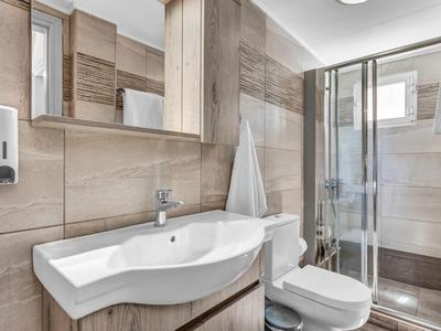 Modernes Hotelbad mit beigen Fliesen, weißem Waschbecken, Dusche und Toilette.