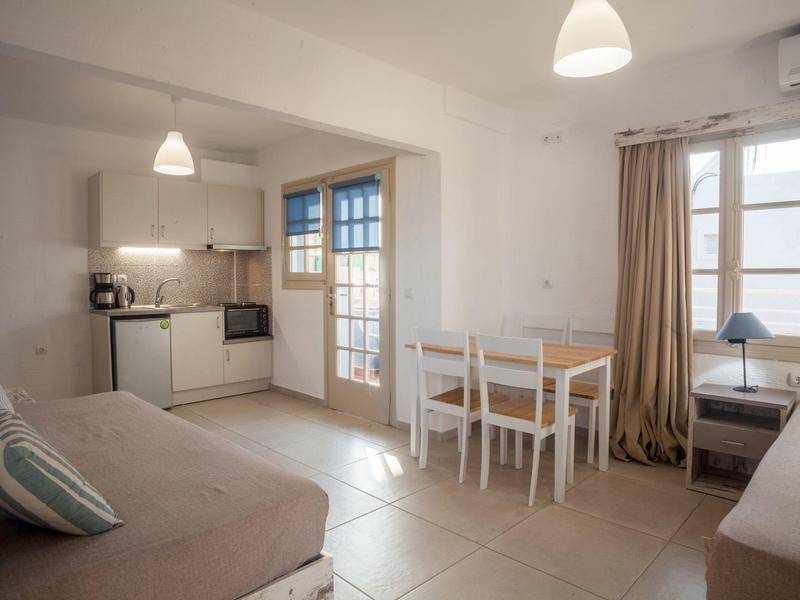 Helle, kompakte Wohnküche mit Schlafsofas, Esstisch, weißen Möbeln und großen Fenstern.