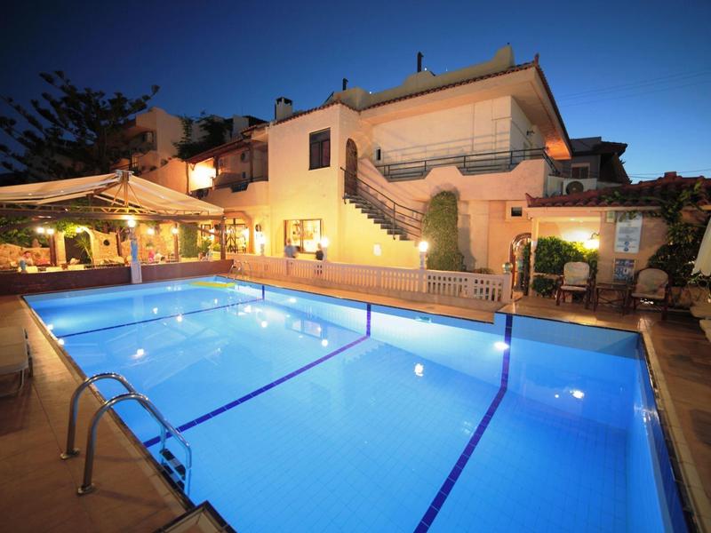 Ein beleuchteter Außenpool vor einem zweistöckigen Haus mit Terrasse und Garten bei Abenddämmerung.