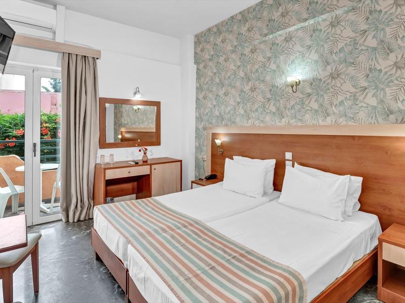 Hell eingerichtetes Hotelzimmer mit Doppelbett, Schreibtisch und Balkon mit Gartenblick.