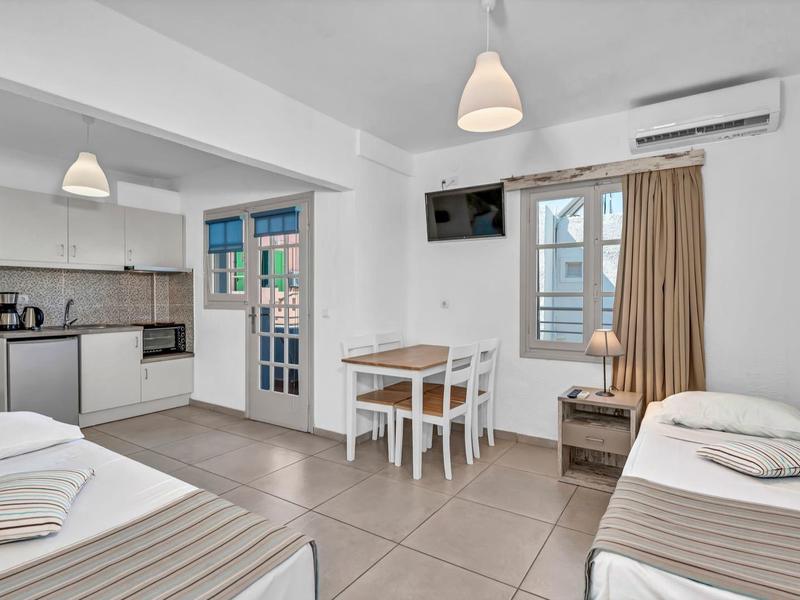 Helles Hotelzimmer mit zwei Einzelbetten, Essbereich, Küchenzeile und Balkon mit Meerblick.