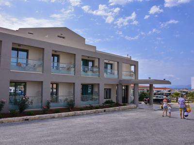 Bâtiment d'hôtel de deux étages avec balcons et deux personnes sur le parking sous un ciel bleu.