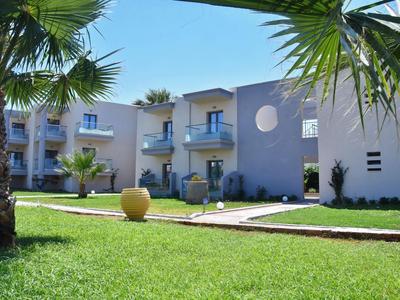 Complexe hôtelier moderne avec jardin soigné et palmiers sous un ciel bleu.