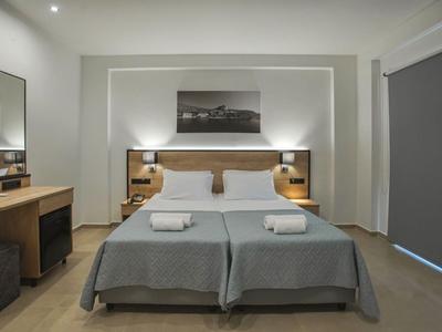 Modern hotel room with two single beds, gray bedding, and minimalist decor.