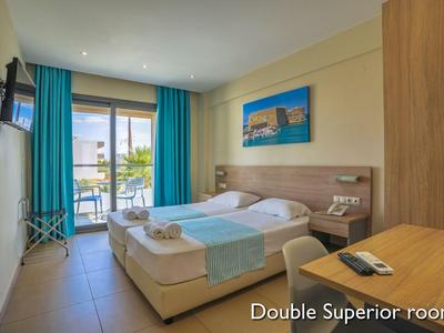 Helles Doppelzimmer mit zwei Betten, blauen Vorhängen und Balkon mit Meerblick.