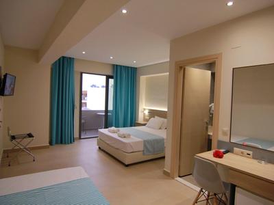 Světý hotelový pokoj se dvěma postelemi, stolem, TV a přístupem na balkon.