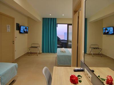 Jednoduchý hotelový pokoj s psacím stolem, židlí, postelí a balkonem s výhledem na západ slunce.