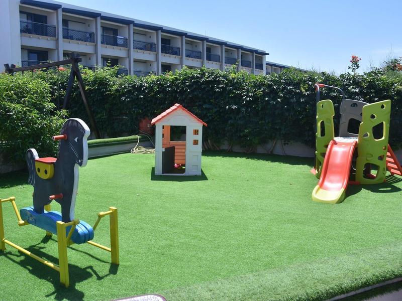 Dětské hřiště s klouzačkou, kolotočem a domečkem na zelené trávě před hotelem