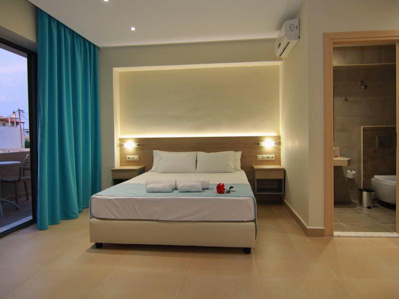 Moderní hotelový pokoj s manželskou postelí, balkonem a otevřenou koupelnou se sprchou.