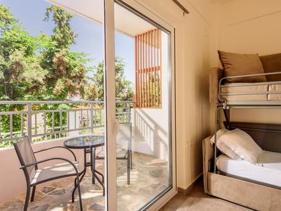 Helles Zimmer mit Etagenbett und Balkon mit Gartentisch und Stühlen, grüne Bäume draußen sichtbar.