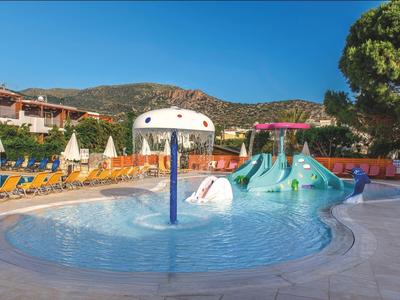 Kinderbecken mit Wasserrutsche und Pilz-Wasserspender, umgeben von Liegestühlen und Bergen.