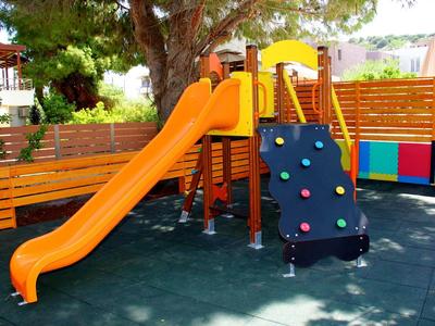 Kinderspielplatz mit orangefarbener Rutsche, Kletterwand und Holzstruktur unter einem Baum.