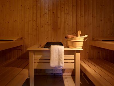 Holzsauna mit Hockern, Eimer und Kelle, Handtuch hängt am Hocker, warme Beleuchtung.
