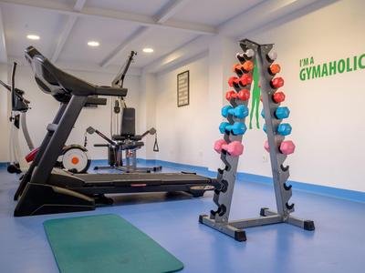 Ein heller Fitnessraum mit Laufband, Hanteln in verschiedenen Farben und grünem Yoga-Matte.
