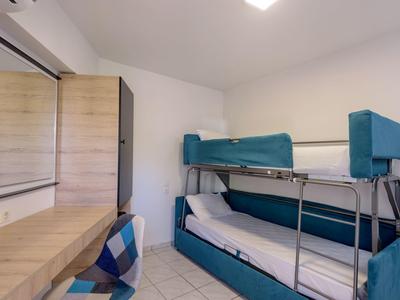 Kleines Zimmer mit Etagenbett, Holzschrank, großem Spiegel und Holztisch mit kariertem Hocker.