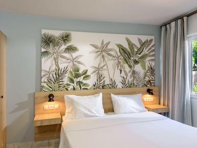 Modernes Schlafzimmer mit großem Bett, Palmen-Wandbild und zwei Nachttischlampen.