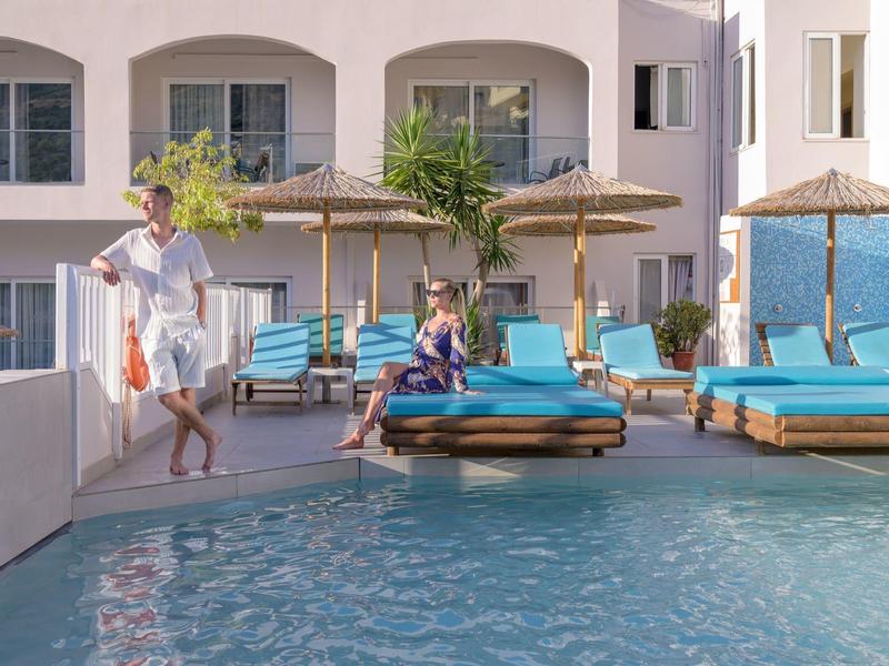 Modern hotelzwembad met blauwe ligbedden en parasols naast een gebouw met twee verdiepingen.