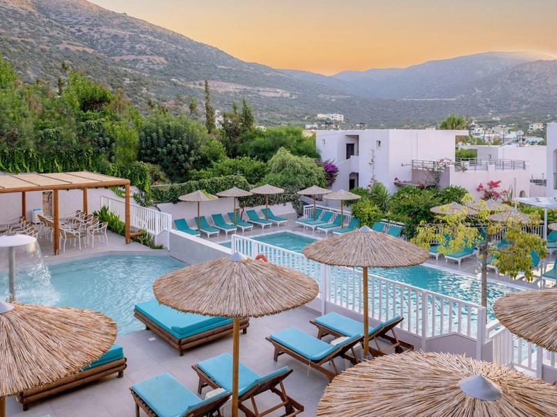 Hotelzwembad met ligstoelen en parasols bij bergen tijdens zonsondergang.