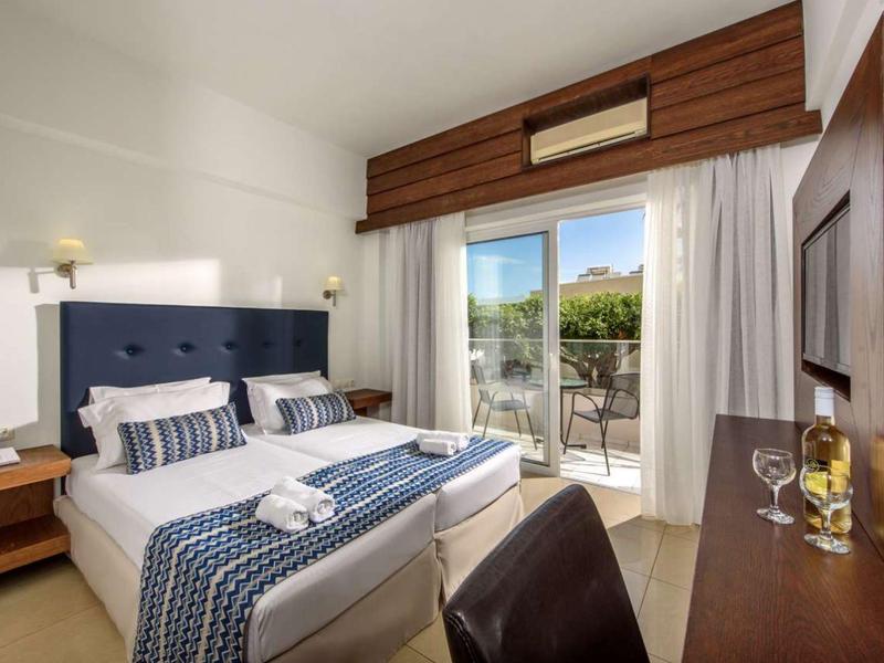 Modern hotelkamer met tweepersoonsbed, bureau en balkon met uitzicht op tuin.