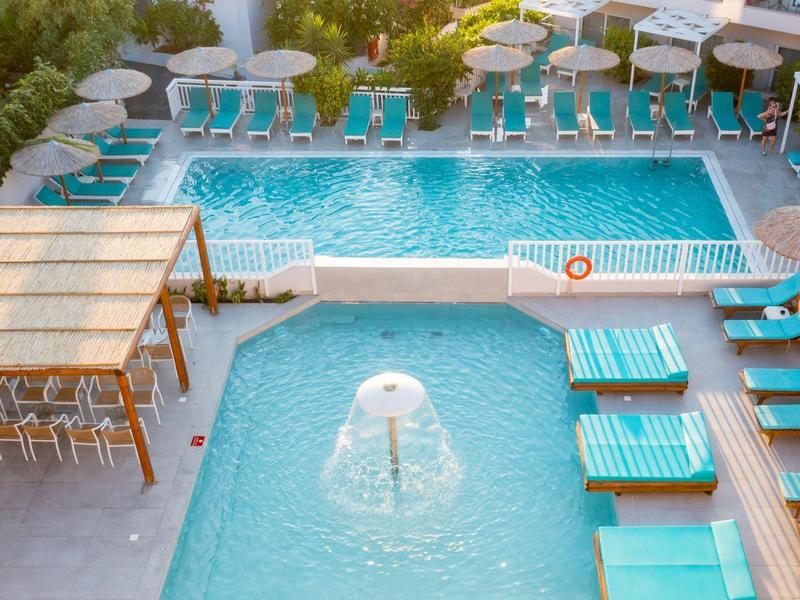 Modern hotelzwembad met twee verbonden zwembaden, parasols en ligstoelen in een lichte omgeving.