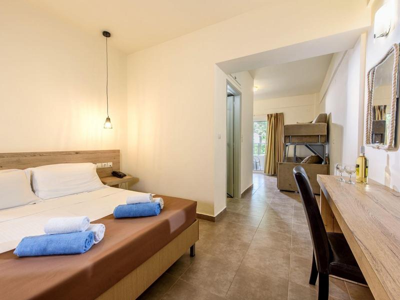 Lichte hotelkamer met tweepersoonsbed, blauwe opgevouwen handdoeken en werkplek met stoel.