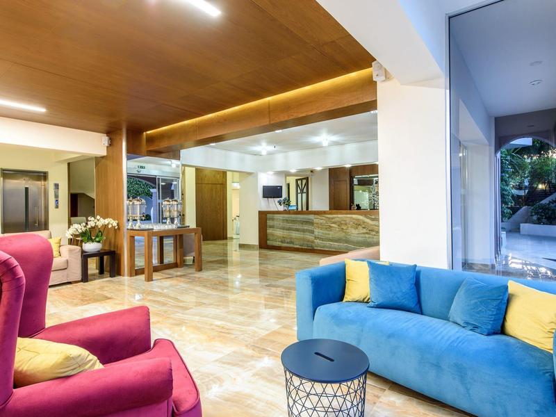 Lichte hotellobby met kleurrijke banken, groot raam en houten receptiebalie.