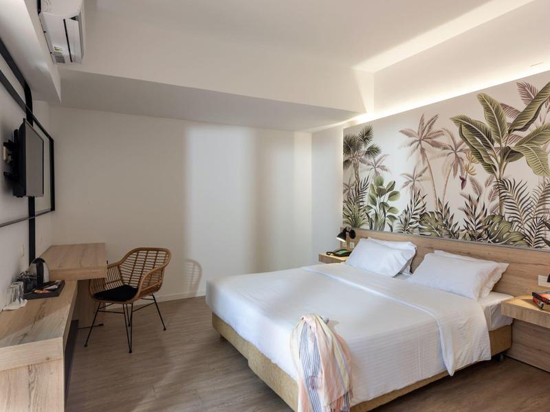 Modern hotelkamer met tweepersoonsbed, bureau, stoel en grote plantdecoratie aan de muur.