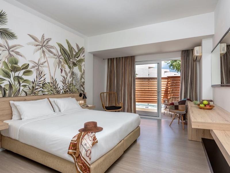 Modern hotelkamer met tweepersoonsbed, plantenmuur, bureau en toegang tot balkon.