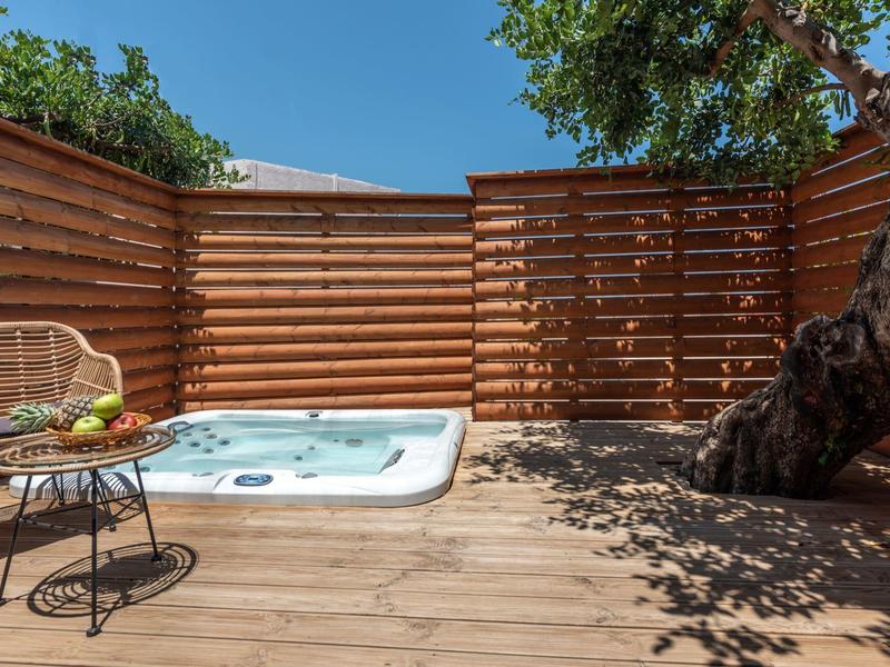 Privé houten terras met jacuzzi, tafel en stoelen naast een boom.