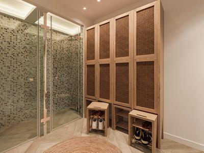 Moderner begehbarer Kleiderschrank mit Holzschränken, Glasdusche und rundem Teppich aus Naturfasern.