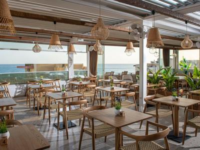 Ristorante aperto con tavoli in legno e vista sul mare in una giornata di sole.