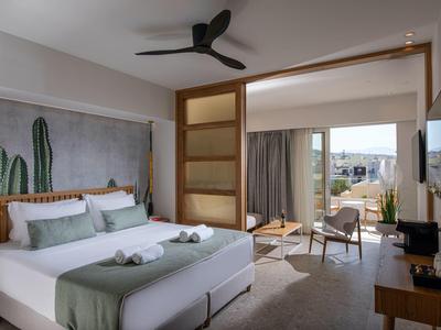 Camera d'hotel luminosa con letto matrimoniale, zona salotto e vista su terrazza e paesaggio.