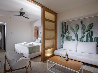 Camera d'hotel moderna con letto matrimoniale, divano e quadro con cactus.