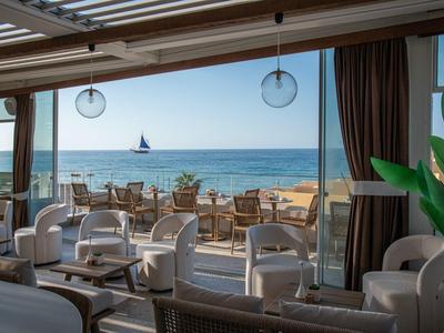 Bar sulla spiaggia luminosa con sedie bianche e vista sul mare e una barca a vela.
