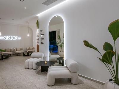 Area lounge moderna e luminosa con sedie comode, tavoli e una grande pianta davanti a una parete bianca.