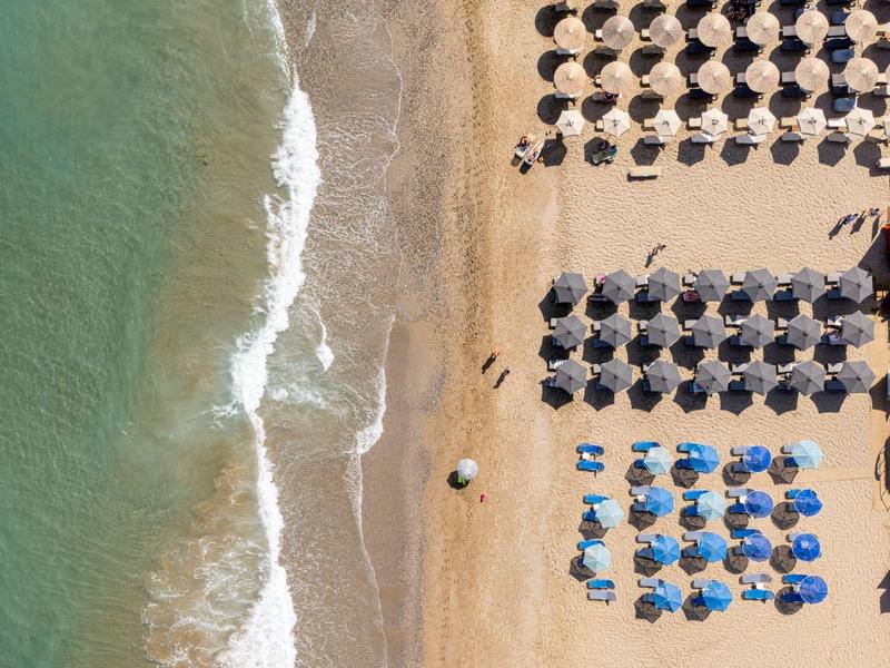 Vista aerea di una spiaggia sabbiosa con onde e file di ombrelloni.