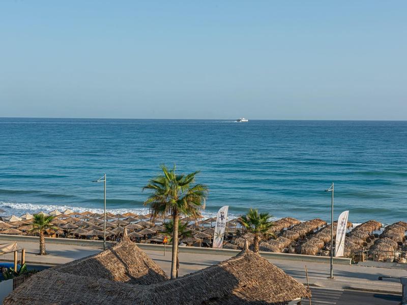Vista sul mare con palme, sedie a sdraio e cielo limpido sulla spiaggia.
