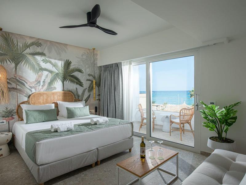 Camera d'hotel moderna con letto matrimoniale, design tropicale delle pareti e balcone con vista mare.