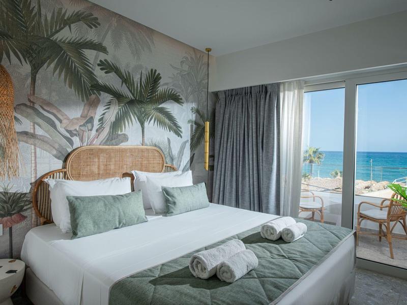 Camera d'albergo moderna con letto matrimoniale, murale tropicale e vista mare dal balcone.