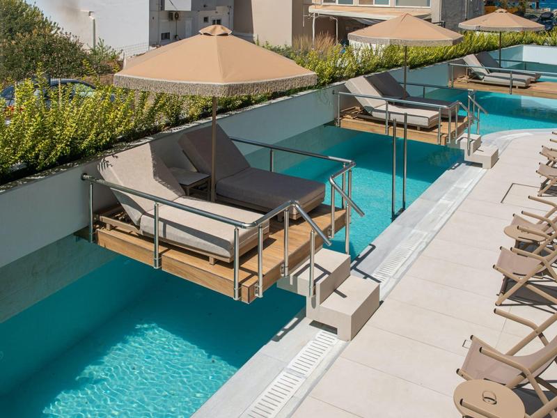 Area piscina con sedie sospese sull'acqua e lettini lungo il bordo piscina.