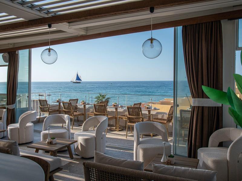 Area salotto moderna con vista mare e barca a vela all'orizzonte in una giornata soleggiata.